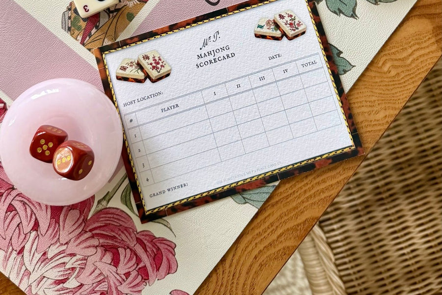 A pink glass dice cup and a mahjong scorecard on the game table